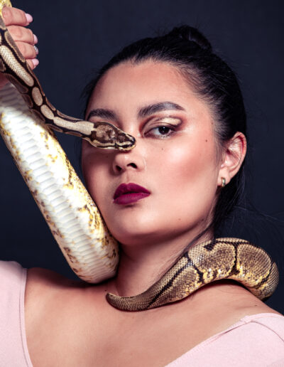 Modèle féminin avec un serpent au niveau du visage sur fond uni.