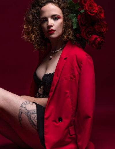 Modèle féminin assise sur un fond rouge avec des roses à la main.